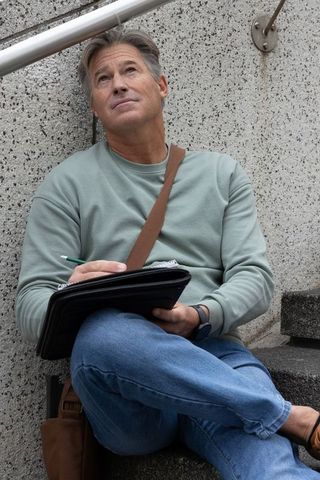 Middle-aged man sitting on urban steps writing in folio, contemplative sketching moment