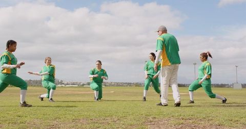 Female softball team warming up with coach on field