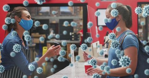 Masked barista serving customer at cafe with covid-19 precautions