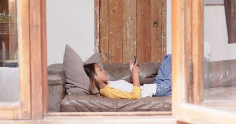 Asian Woman Relaxing with Smartphone on Leather Sofa in Modern Home