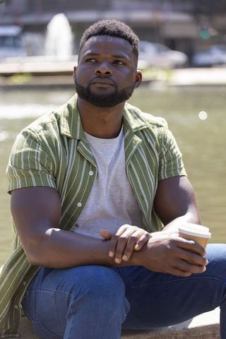 Contemplative man sitting by urban fountain holding takeaway coffee, gazing thoughtfully