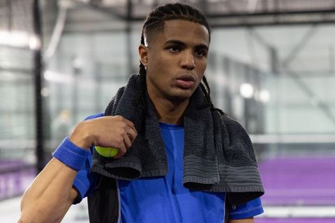 Focused tennis player resting with towel and ball on indoor court during training session
