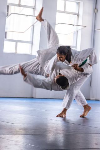 Teenage girl practicing martial arts throw technique in dojo