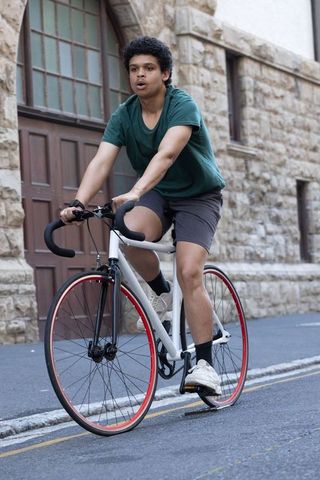 Urban african american cyclist pedaling white fixed-gear bike past stone archway