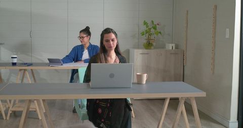 Indian woman working on laptop in modern coworking space with colleague using tablet
