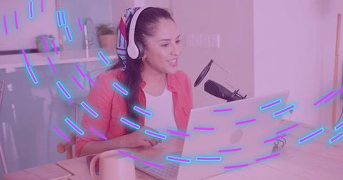 Recording host broadcasting podcast from bright home studio with laptop and microphone