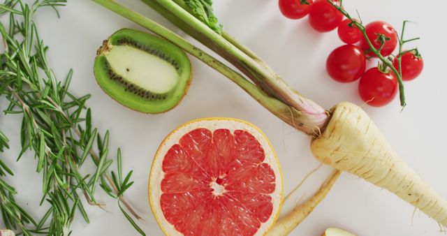 photo displaying a variety of fresh fruits and vegetables including a halved kiwi, a sliced grapefruit, cherry tomatoes on the vine, sprigs of rosemary, and whole parsnips. This arrangement highlights the vibrant colors and natural texture of raw, organic produce. Ideal for use in healthy eating blogs, dietary guideline publications, food magazine editorial layouts, and grocery store advertisements.