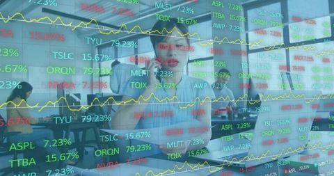Female finance analyst taking call tracking live market data typing trades modern office