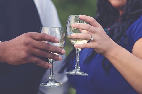 Couple clinking wine glasses showcasing engagement ring during romantic celebration
