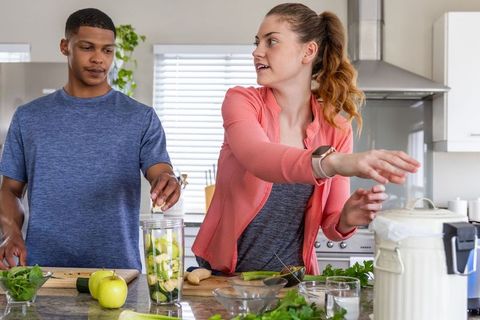 Couple preparing green smoothie with apples cucumber and herbs at modern kitchen