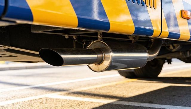Close-up of chrome exhaust tip and muffler under commercial vehicle with yellow blue stripes