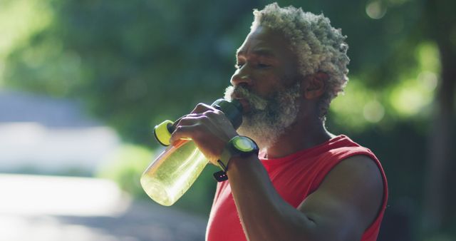 African american senior man exercising outdoors drinking from water bottle in street. healthy retirement and active lifestyle.