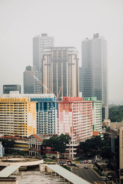 Bright, colorful apartment complex stands out against backdrop of tall, modern commercial skyscrapers. Suitable for illustrating urban architecture, contrast of old and new infrastructure, and vibrant city living in Asian metropolises. Can be used in articles or publications related to city development, real estate, or architecture in Singapore.