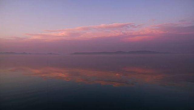 Pastel Dawn Over Calm Sea Reflecting Pink Clouds and Misty Island Silhouettes