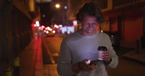 Smiling Man Using Smartphone and Drinking Coffee at Night in City