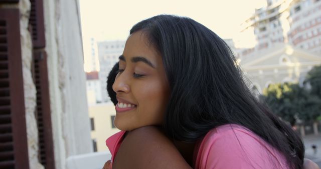 A young African American woman is smiling while embracing someone, with copy space. Her expression conveys happiness and affection in an urban setting.