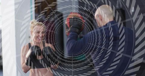 Female athlete training boxing while coach holding focus mitts, smiling and focused