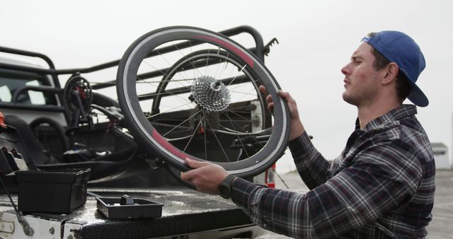 Man focusing on repairing a bicycle wheel outdoors, holding it with both hands. Tool box indicates maintenance work. Useful for content related to sports, cycling, DIY bicycle repairs, outdoor activities, and active living.