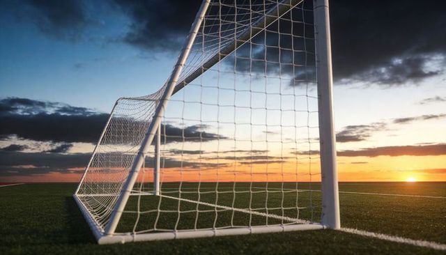 Framing sunset soccer goal on artificial turf with white goal line, net, dramatic dusk horizon