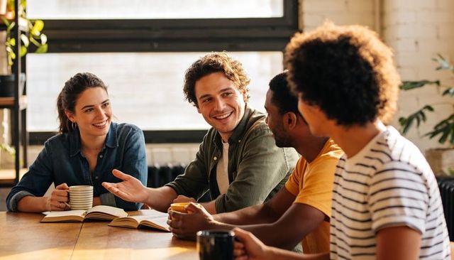 Young professionals sharing ideas, smiling at wood table in bright coworking space
