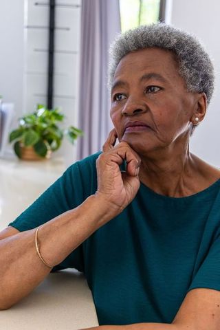 Senior african woman resting chin on hand reflecting at home with potted plant