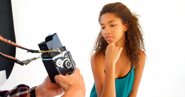 Teenage girl curiously observing a classic camera being shown by a photographer in a studio. Useful for themes related to photography education, learning new skills, youth engaging in creative arts, modeling, and studio photography. Great for articles, blogs, educational materials, and advertisements promoting engagement in photography.