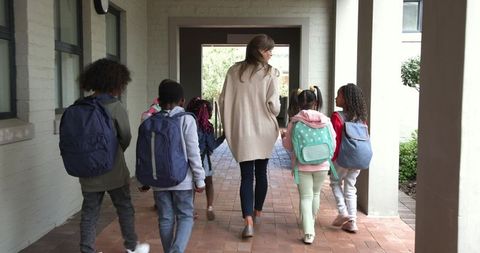 Teacher leading children with backpacks in school corridor