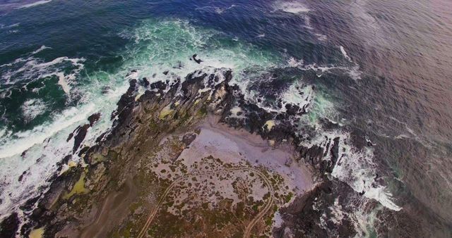 This image presents a stunning aerial perspective of a rocky coastline with waves crashing against it. Shows drama and beauty of nature, suitable for use in travel brochures, environmental awareness campaigns, coastal tourism advertisements, and nature-centric website backgrounds.