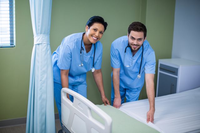 Portrait of male and female nurse preparing bed for patient in ward
