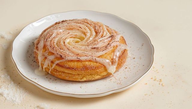 Glazed cinnamon swirl danish on gold-rim porcelain plate with delicate glaze drizzle