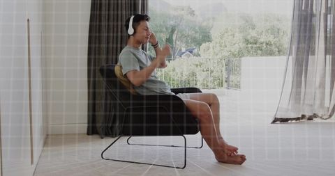 Asian man relaxing with wireless headphones in modern lounge chair overlooking balcony view