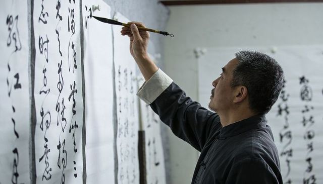 Traditional calligrapher practicing brush script on hanging paper scrolls in studio