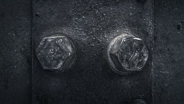 Glinting hex bolts on worn steel plate with corrosion and water droplets macro texture