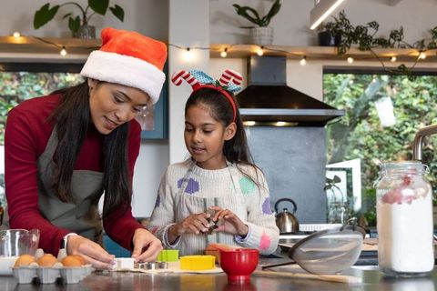 Indian mother and daughter baking christmas cookies wearing santa hat and festive headband
