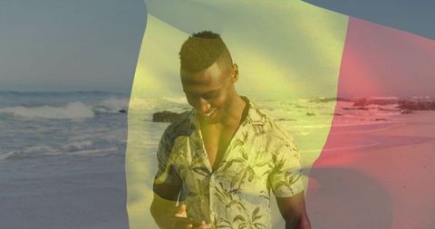 Man using smartphone on tropical beach with tricolor flag overlay, sunlit coastal vibes