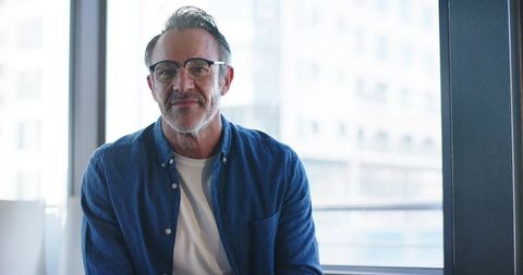 Mature Professional Sitting by Office Window Smiling Confidently in Urban Workspace
