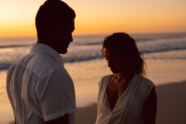 Young couple standing close together on beach during sunset, creating a romantic and serene atmosphere. Ideal for use in travel brochures, romantic getaway promotions, relationship blogs, and lifestyle magazines.