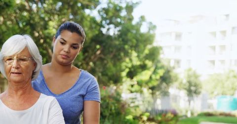 Caregiver Assisting Senior Woman Walking on Garden Path in Residential Courtyard