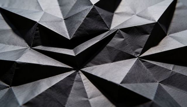 Radial folded black paper forming geometric triangular facets origami tessellation texture