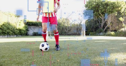 Teen soccer player standing with ball near goal wearing yellow bib red kit on grass pitch