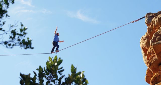 Man skillfully balancing on highline stretched between cliffs outdoors. Conveys themes of adventure, extreme sports, bravery, and skill. Suitable for articles or media related to extreme sports, outdoor activities, self-improvement, courage, and physical fitness.