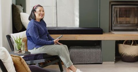 Smiling Mature Asian Woman Using Tablet in Cozy Modern Living Room