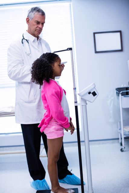Doctor measuring height of young girl in clinic. Ideal for illustrating pediatric healthcare, medical checkups, growth monitoring, and child wellness. Useful for health-related articles, pediatric care brochures, and educational materials on child development.