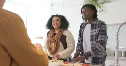 Mid adult couple preparing vibrant vegetable salad on kitchen island in bright modern home