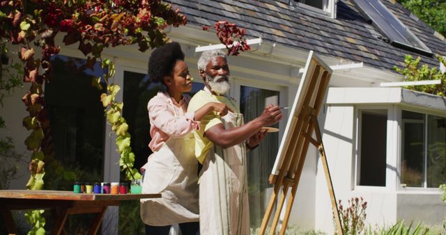 African american couple talking in sunny garden man painting picture on a canvas. staying at home in isolation during quarantine lockdown.