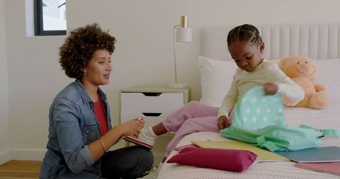 Mother Guiding Daughter in Packing Backpack for School