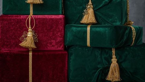 Stacking burgundy and emerald velvet gift boxes gleaming with gold tassels and ribbons
