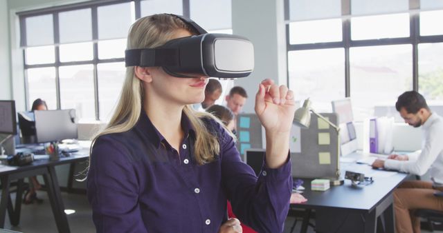 Woman using virtual reality headset in modern office with colleagues working in the background. Ideal for promoting cutting-edge technology in business, digital transformation, and innovative office environments.