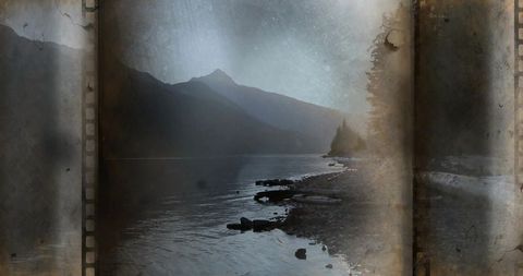 Misty mountain lake shoreline with driftwood, pebble beach and vintage film sprocket effect