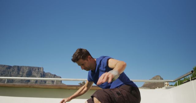 Engage viewers with this dynamic image of an active man showing off skateboarding skills on a rooftop under a clear, sunny sky. Ideal for promoting healthy, active lifestyles, outdoor sports, or leisure activities. Suitable for use in health and fitness blogs, sportswear advertisements, or urban lifestyle websites.